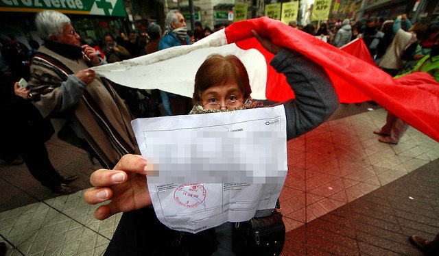 Manifestante con la bandera de Chile muestra una liquidación de pago de pensión; los datos personales del documento están difuminados